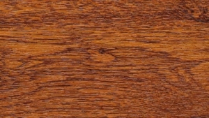 Close-up of a polished oak wood surface with visible grain patterns and warm brown tones.
